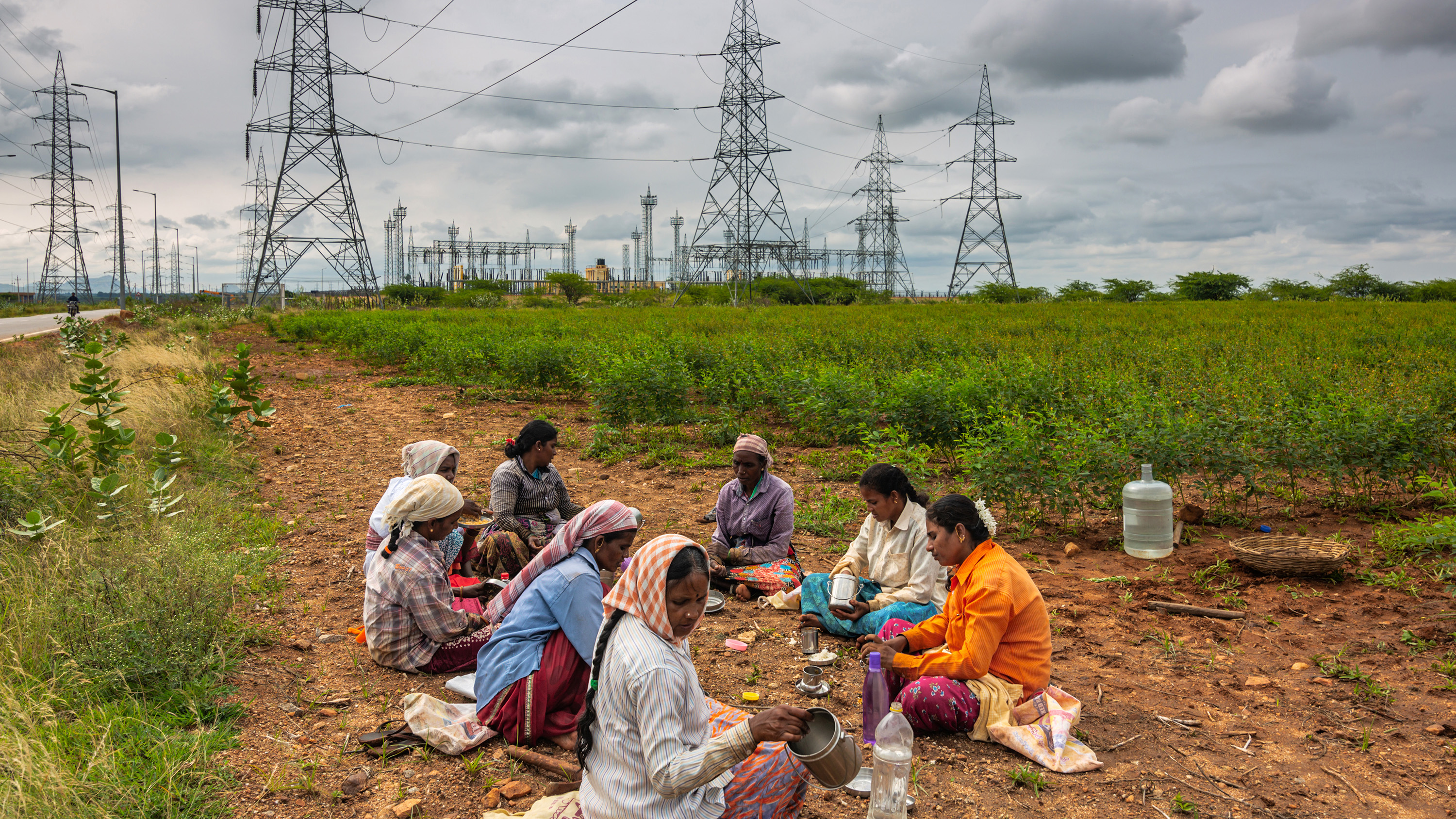 Kvinnor äter sin frukost under elektriska pyloner byggda för att överföra el som genereras i Pavagada Solar Park