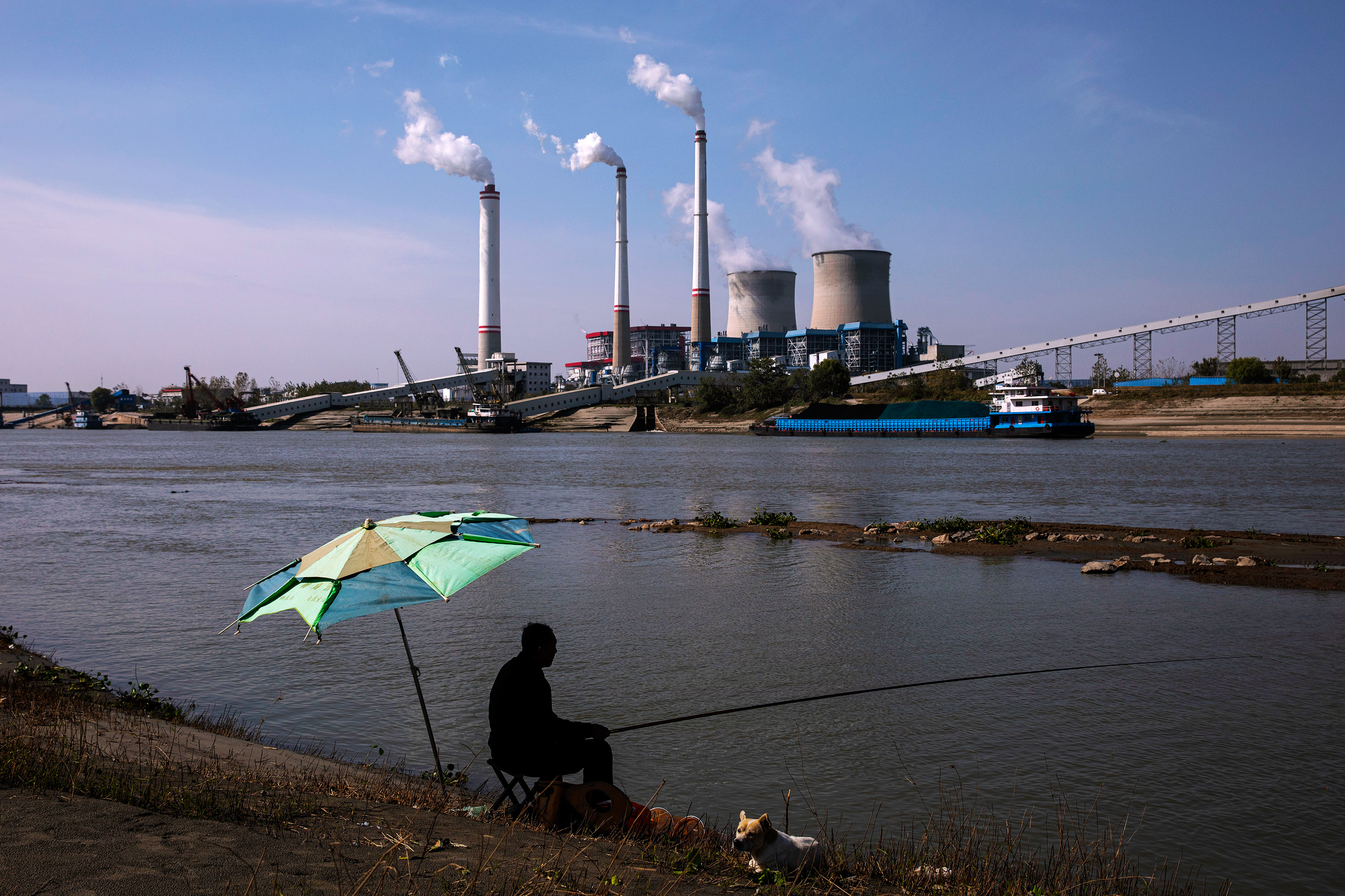 Beboer sidder ved floden og fisker som kulfyret kraftværk