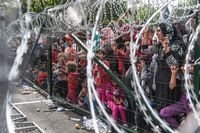 Vluchtelingen staan achter een hek bij de grens tussen Hongarije en Servië.